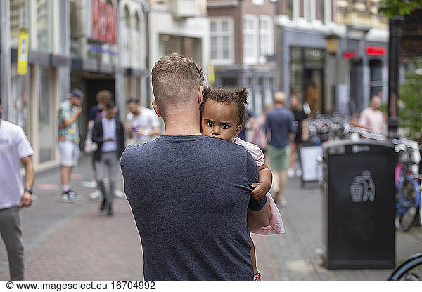 A caucasian father carries his daughter through the streets of Utrecht