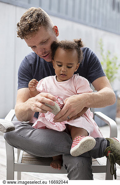 A caucasian father helps his biracial daughter put her shoes on