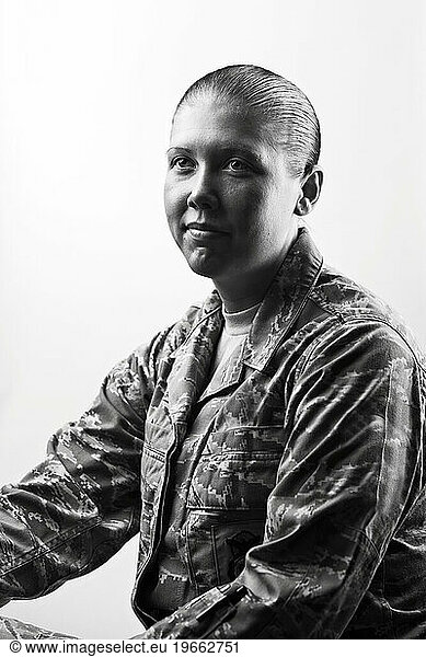 A Caucasian  female  Air Force Security Forces Airman in uniform sits for a black and white portrait with a white backdrop.