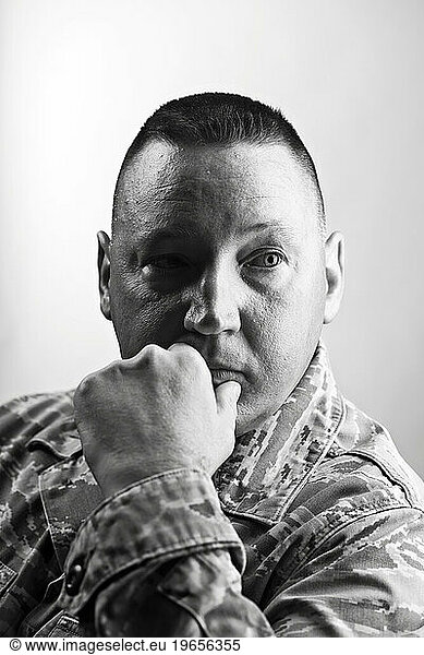 A Caucasian  male  Air Force Security Forces Airman in uniform sits for a black and white portrait with a white backdrop.