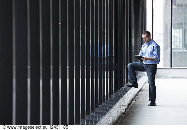 A Caucasian male architect standing by a wall of windows  using a digital tablet.