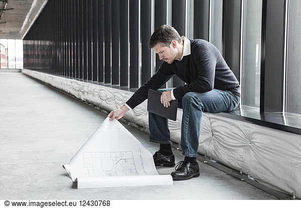 A Caucasian male architect working on building plans in a new raw business space.