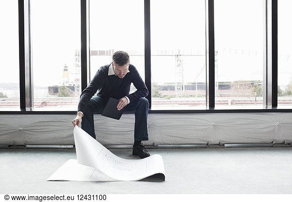 A Caucasian male architect working on building plans in a new raw business space.
