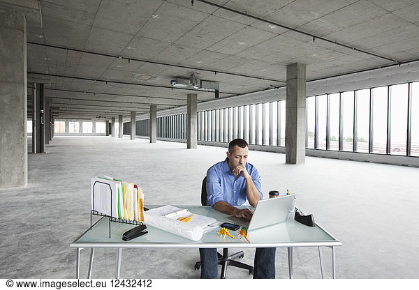 A Caucasian male business owner at his temporary desk in a new raw business space.