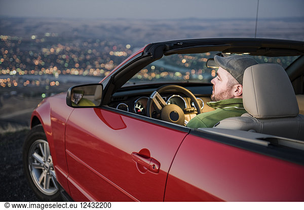 A Caucasian male parked in his convertible sports car watching the sunset over the Clearwater River and the city of Lewiston Idaho.