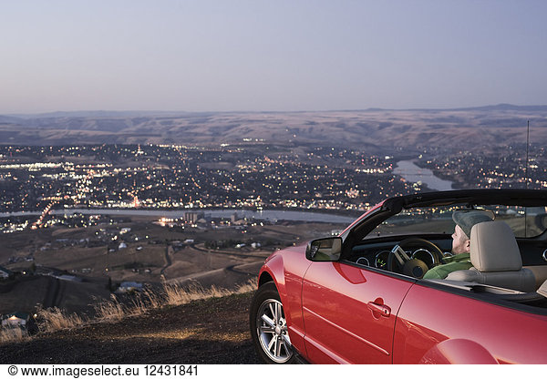 A Caucasian male parked in his convertible sports car watching the sunset over the Clearwater River and the city of Lewiston  Idaho  USA.