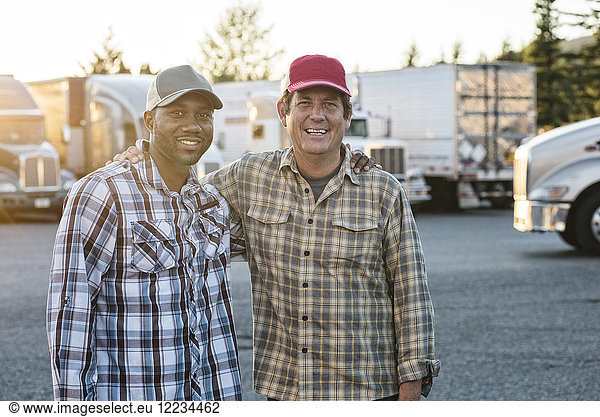 A Caucasian man and a black man truck driving team together in a truck stop parking lot.