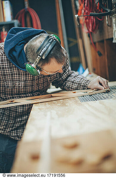 A Caucasian  middle aged man works on a small piece of a wooden airplane in his garage.