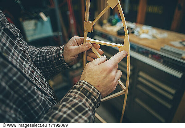 A Caucasian  middle aged man works on a small piece of a wooden airplane in his garage.