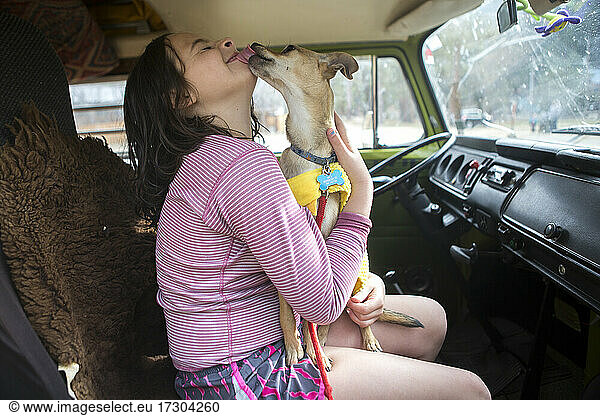 A chihuahua licks girl's face in VW camper van during roadtrip