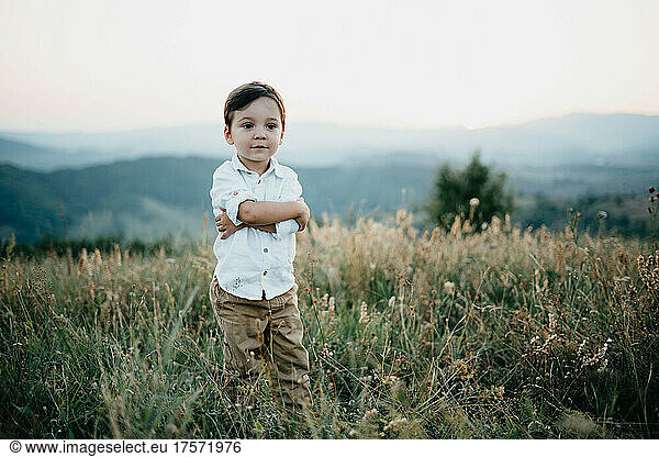 A child boy stands in a field of grass with hands around his waist