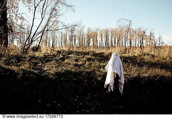 A child in ghost costume running in a park in the fall during the day