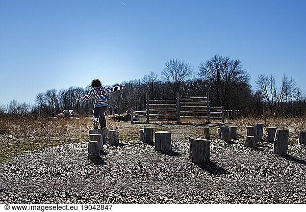 A child leaps across tree stumps in an outdoor obstacle course