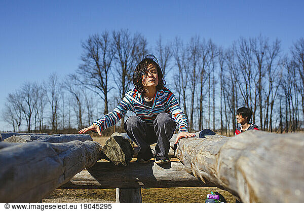 A child perches on wooden structure in park with father in background