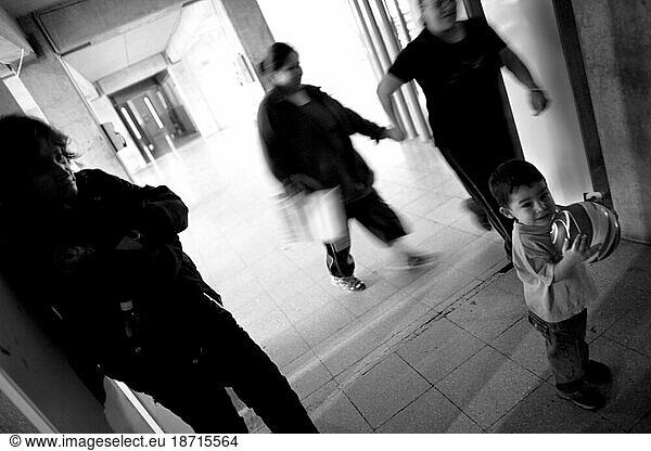 A child plays with a ball in a prison hallway while a guard watches.