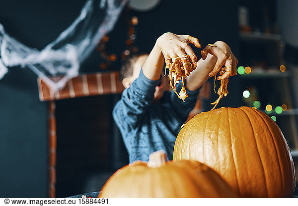 A child pulling their hands out of a pumpkin covered in seeds and pumpkin flesh.
