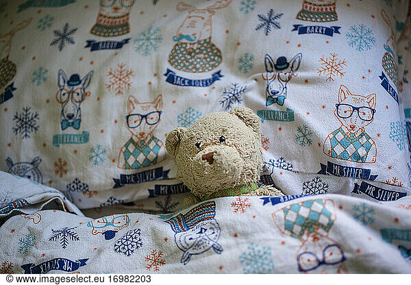 A child's stuffed bear toy lays lovingly tucked into cozy bed