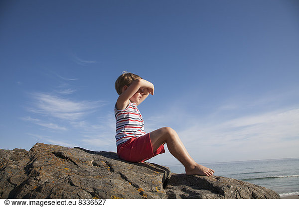 A child seated on the rocks looking out to sea.