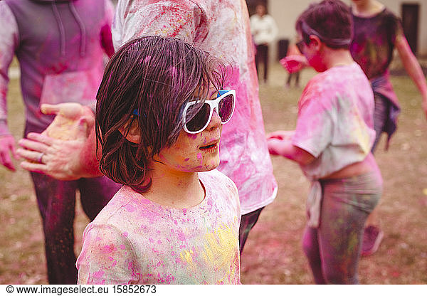 A child stands in crowd covered in colorful chalk celebrating Holi