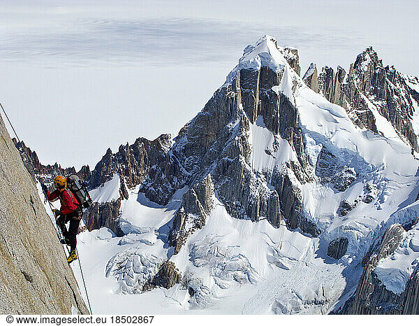 A climber climbs the steep north face of Torre Egger  with the peaks of Cerro Rincon and the glaciers of the Southern Patagonia