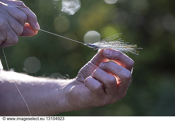 A close up of a fly fisherman tying a new feathery fishing fly onto his line for use in salt water.