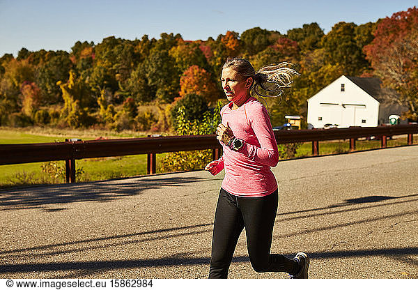 A close up of a woman running down a country road on a fall day.