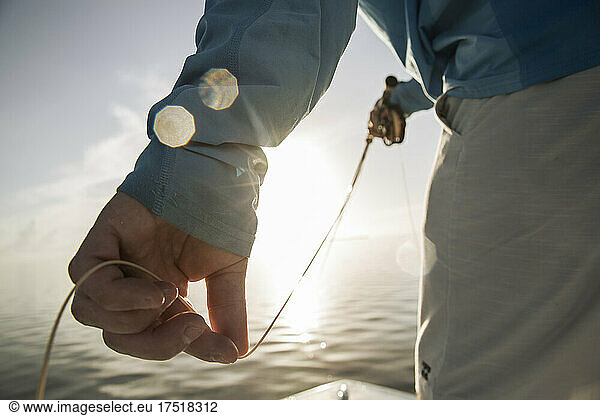A close up of mans fingers holding fly line with sun shining through