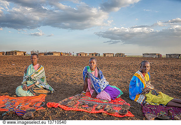 A close up of three Maasai women sitting with their handmade goods and items  hoping to sell some to tourists visiting their village  at Maasai Mara National Reserve in Kenya  Africa.