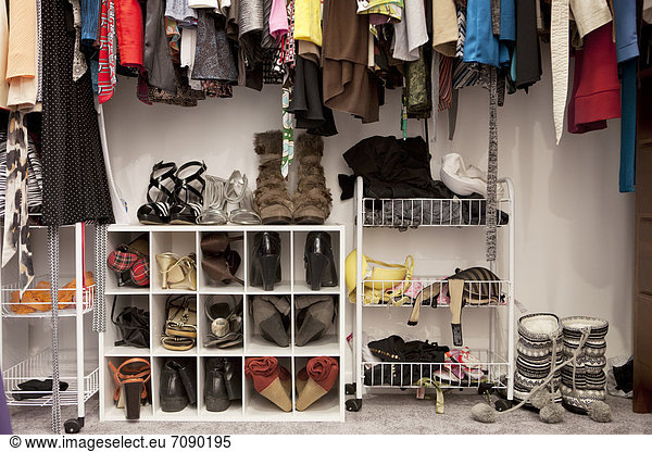 A closet in a bedroom. A large cupboard with organised storage scheme. Clothes hanging on rails  and shoes stacked and stored away. Personal belongings.