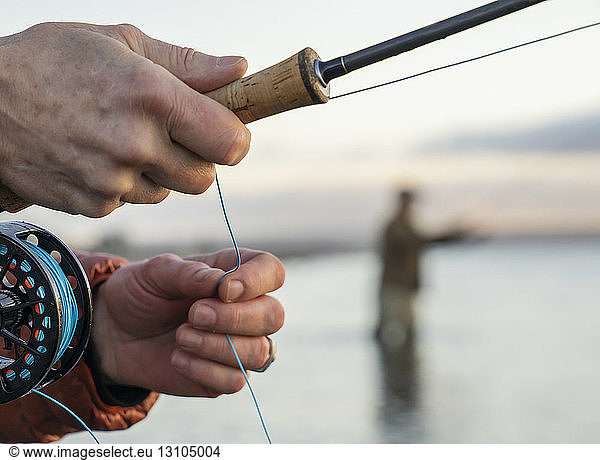 A closeup of a fly fisherman's hands holding his fly rod and line while fishing.