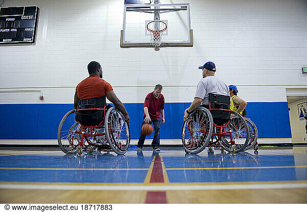 A coach demonstrates ball handling during wheelchair basketball practice.