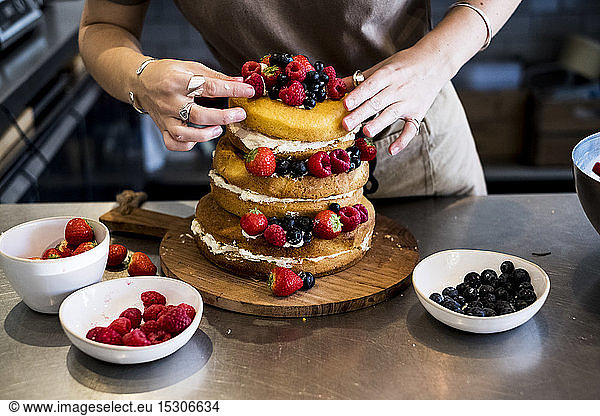 a cook working in a commercial kitchen arranging fresh fruit over a layered cake with fresh cream.