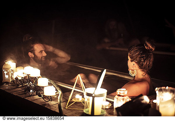 A couple glows in romantic candle light in outdoor bath in nature