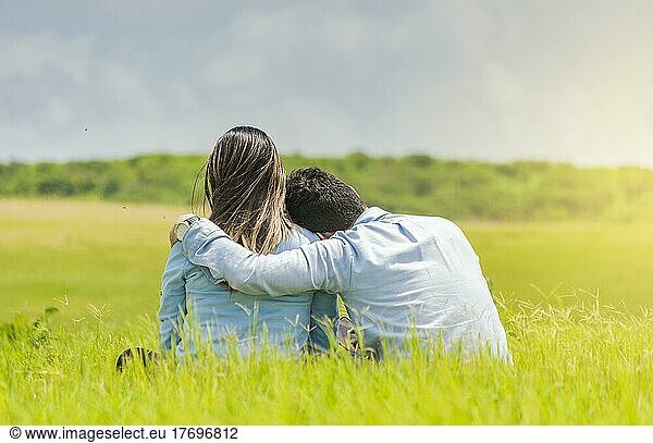A couple in love sitting on the grass hugging from the back  a romantic couple sitting on the grass hugging from the back  rear view of a couple in love hugging on the grass