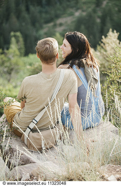 A couple in the mountains, taking a break, sitting on a hillside.