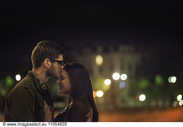 A couple kissing in a city at night.