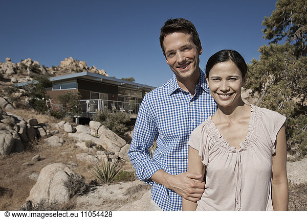 A couple  man and woman and the view of their eco home  designed to blend into the rocky hilllside of a desert landscape. Architecture with a low impact blending into the landscape.