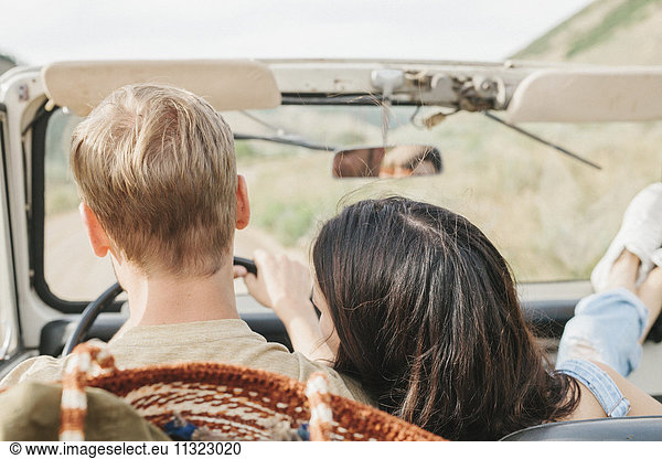 A couple on a road trip in an open top jeep. Rear view