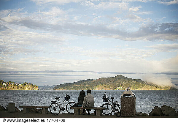 A Couple Sits By San Francisco Bay As The Sun Sets; San Francisco  California  United States Of America