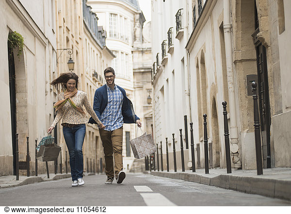 A couple walking along a narrow street in a historic city centre  with shopping bags.