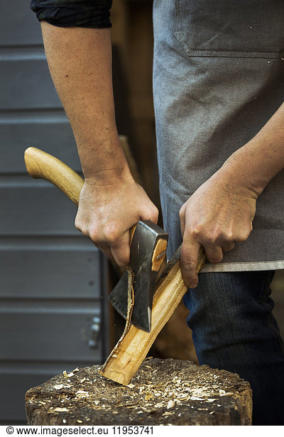 A craftsman holding a small axe  cutting down a small piece of wood on splitting block covered in wood shavings.