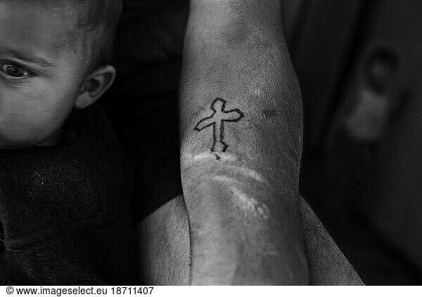A crucifix tattoo on the arm of a man holding a small child.