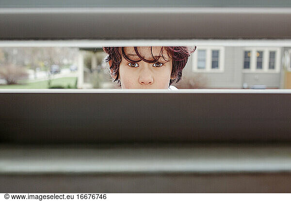 A curious child standing outside peeps into crack of an open window