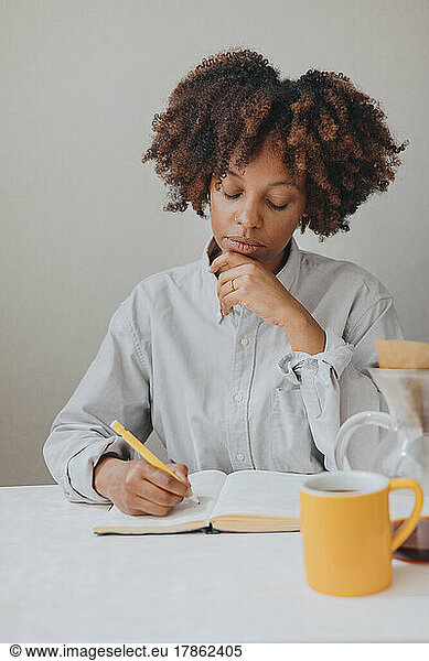 A curly haired woman takes notes in a notebook in the kitchen.