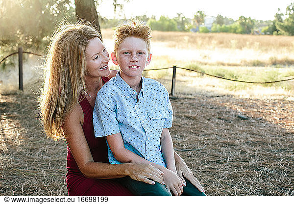 A Cute Boy With Red Hair Sits On His Mother's Lap While Outside