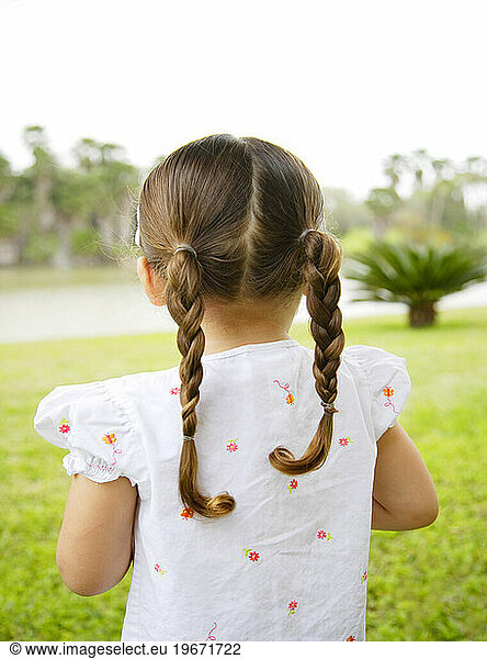 A cute little hispanic girl  with her back to the viewer  in pigtails with a tropical background view.
