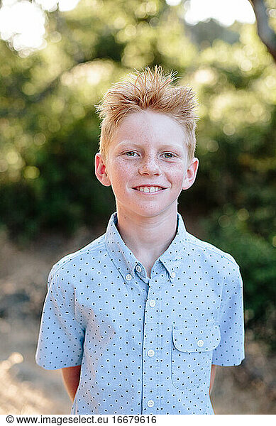 A Cute Red Haired Boy With Freckles Smiles For A Portrait Outside