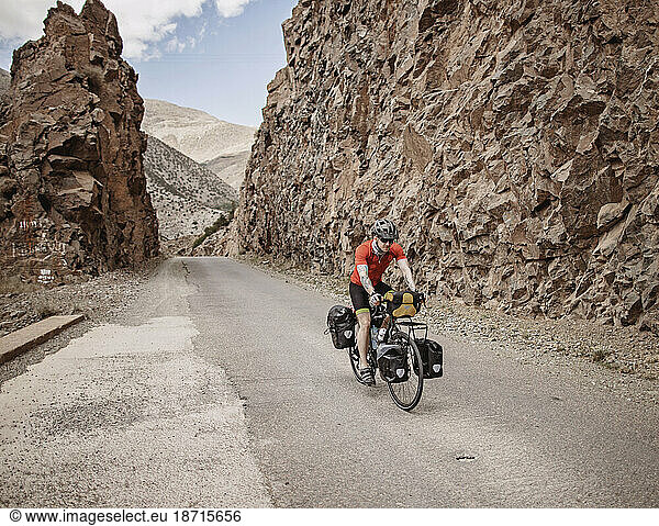 A cyclist rides through a rock cut on a mountain road in Morocco
