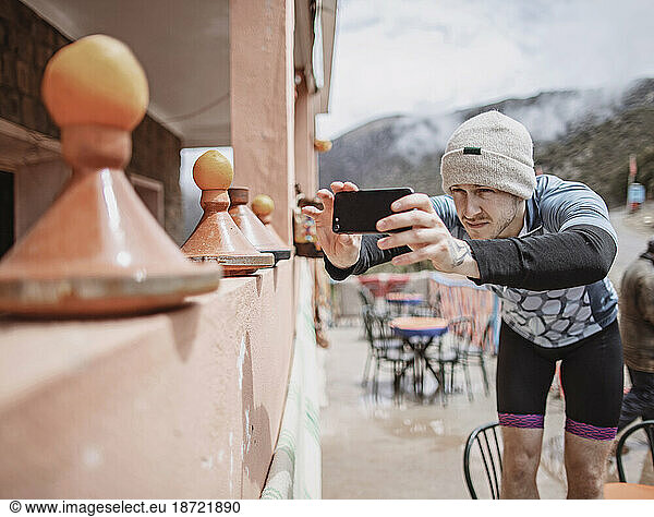A cyclist with a hat takes a cell phone picture of a Moroccan Tagine