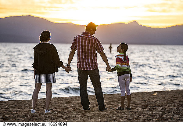 A dad and his daughters watch sunset on the beach in Lake Tahoe  NV